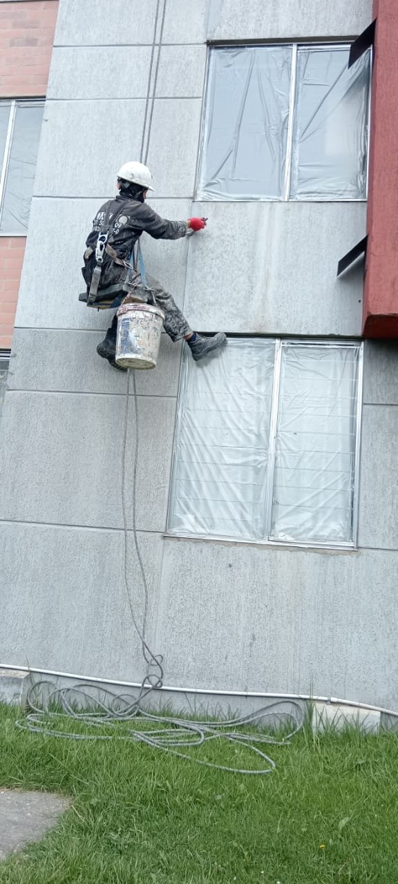 Operario en descuelgue aplicando sobre la fachada con protección plástica