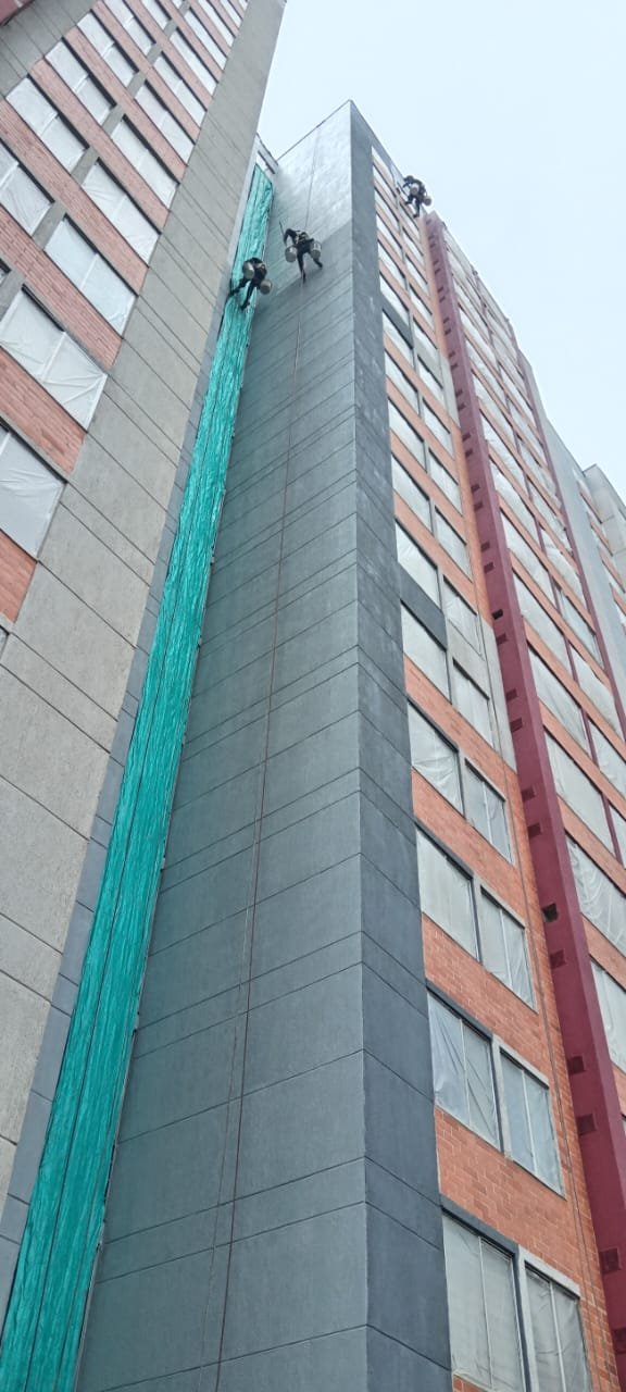 Operario suspendido sobre el paño gris de la fachada