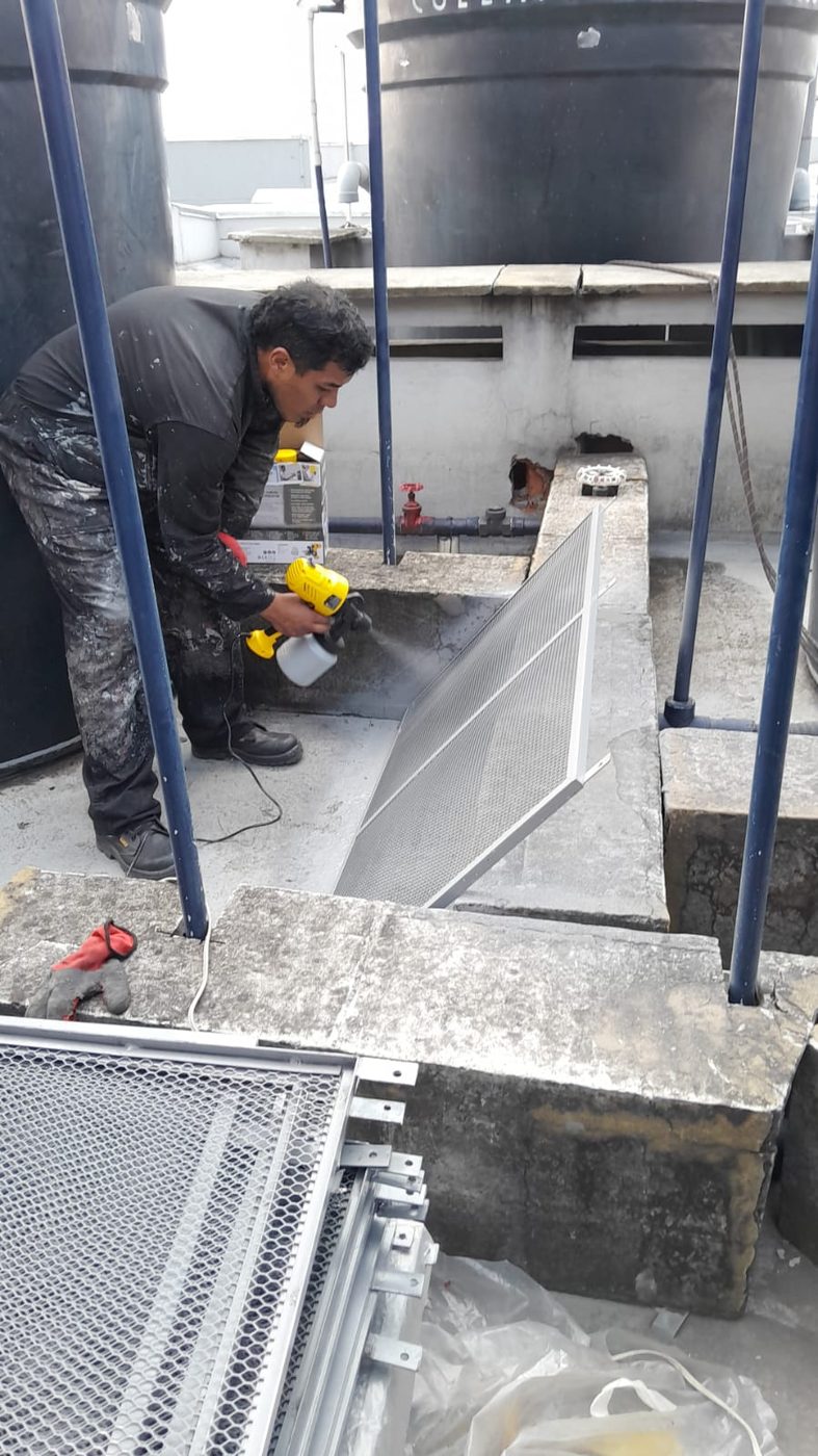 Operario aplicando pintura a una rejilla antes de su instalación